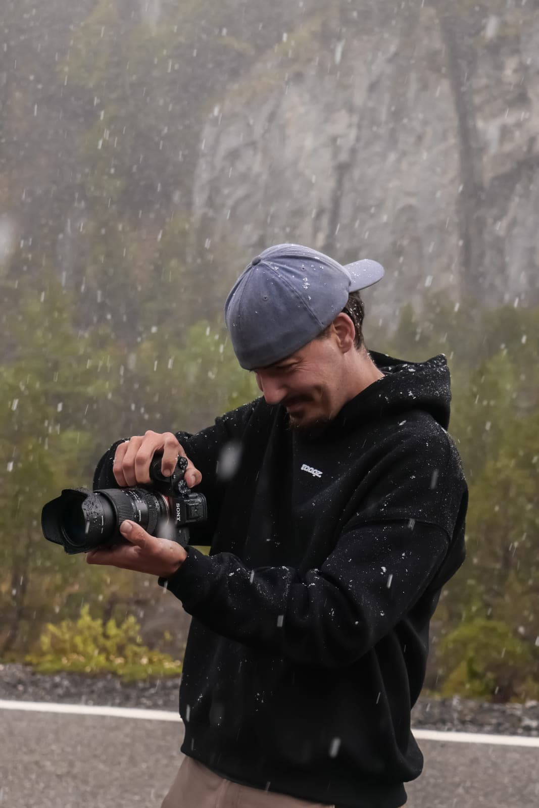 Romain Nicolerat, appareil photo en main, sous la neige au bord d’une route de montagne.