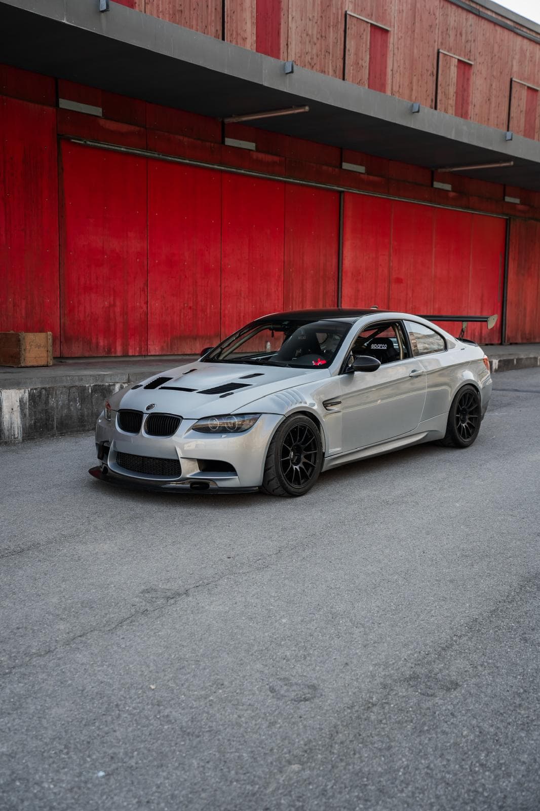 BMW M3 E92 grise de face devant un bâtiment aux volets rouges