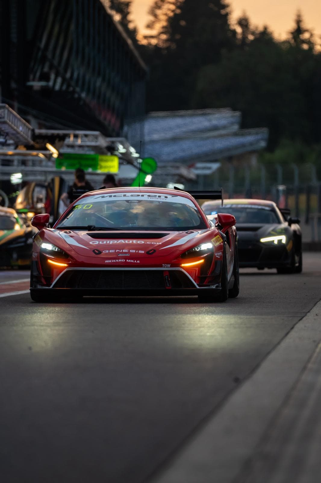 Voitures de course alignées de nuit sur la piste, feux avant allumés
