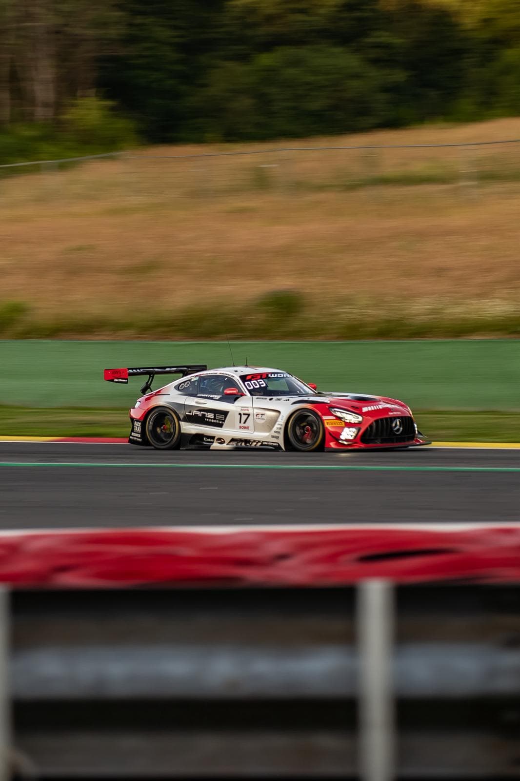 Voiture de course rouge et blanche en filé, arrière-plan de piste flou