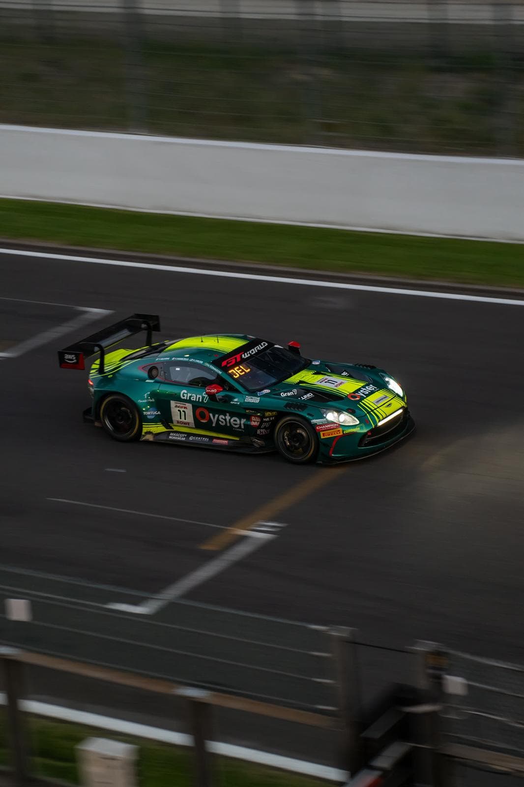 Voiture de course GT verte négociant un virage, vue plongeante sur la piste