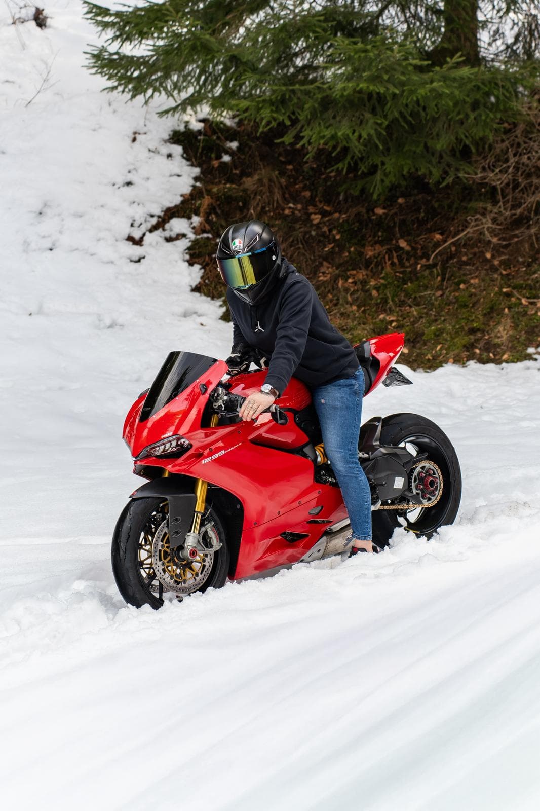 Pilote en appui sur une moto Ducati Panigale rouge, congère au premier plan