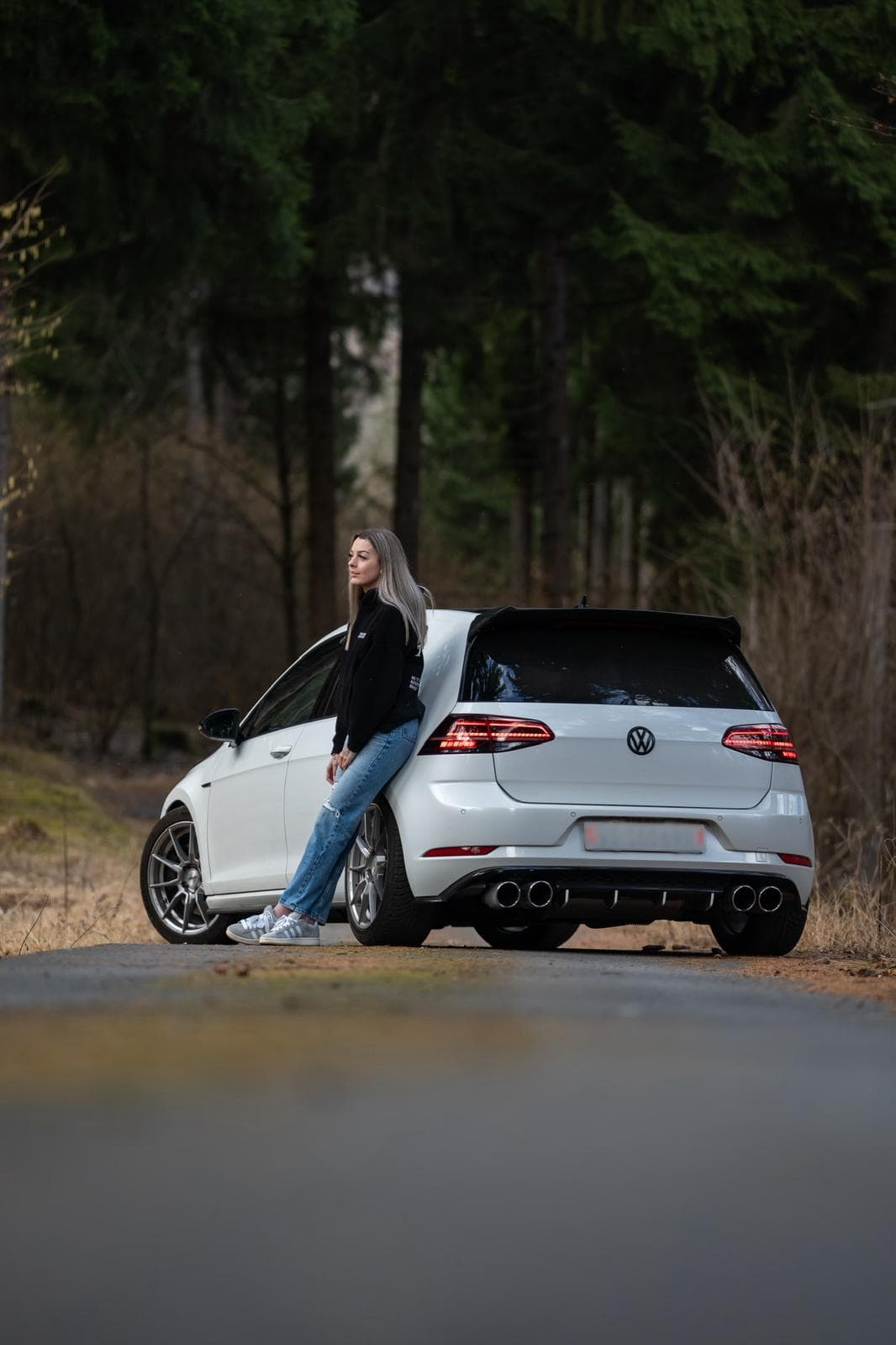 Arrière d'une Volkswagen Golf R blanche en forêt, une personne assise sur le hayon