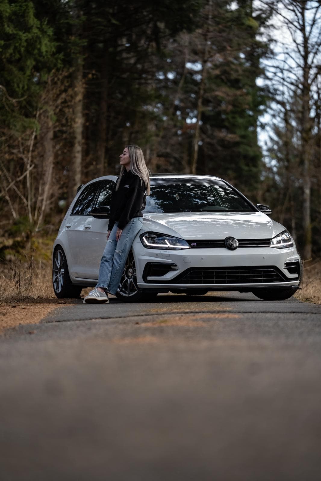 Volkswagen Golf R blanche de face sur une route forestière, une personne appuyée contre l'aile