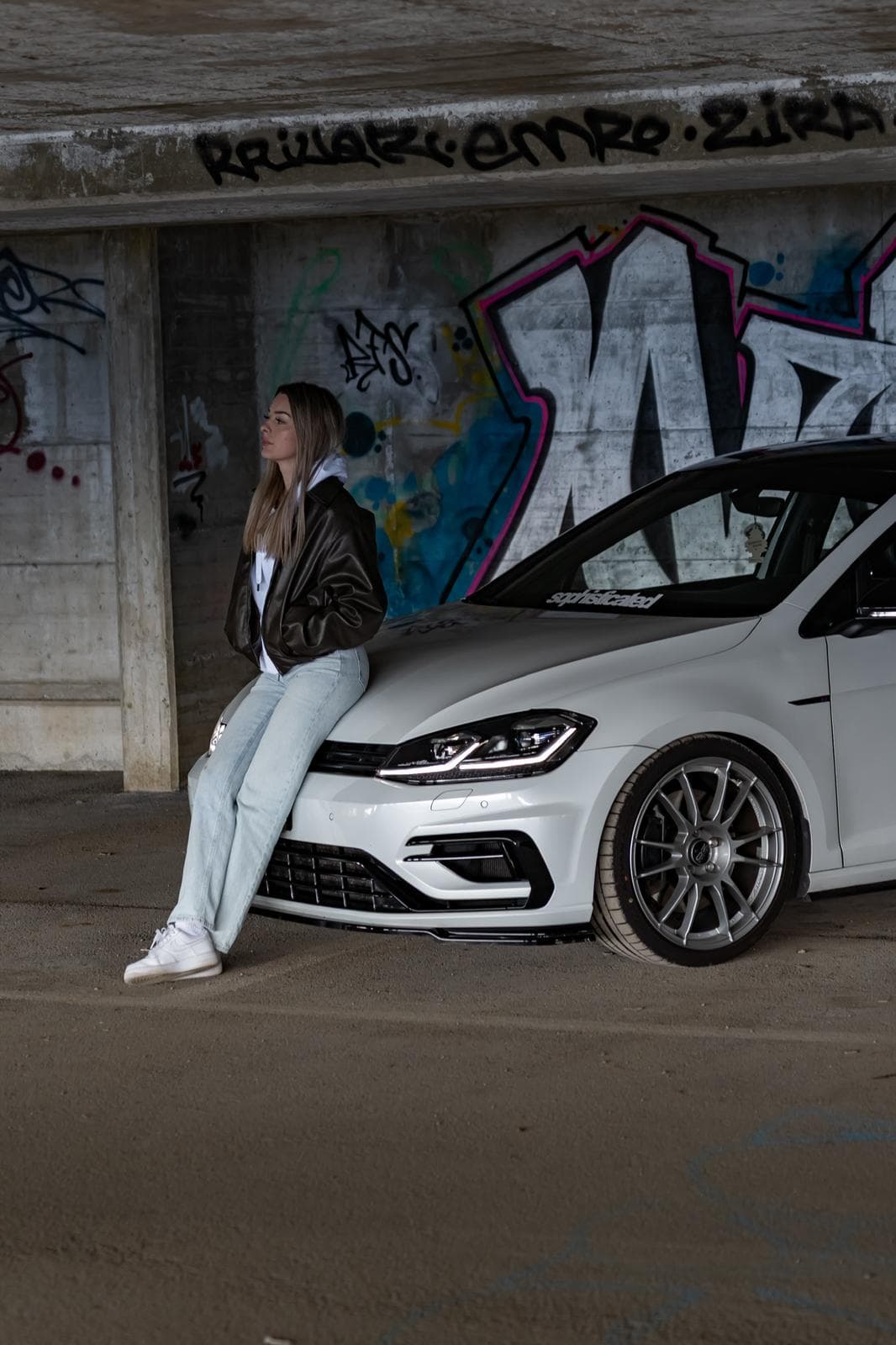 Volkswagen Golf R blanche devant un mur de graffitis sous un pont de béton