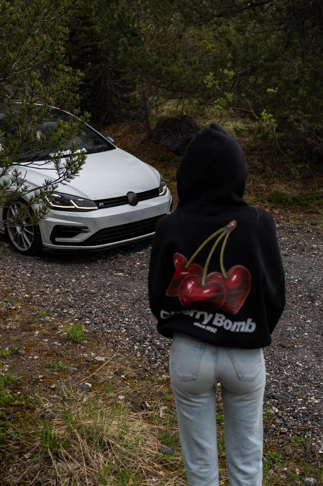 Personne de dos en sweat à capuche devant une Volkswagen Golf R blanche