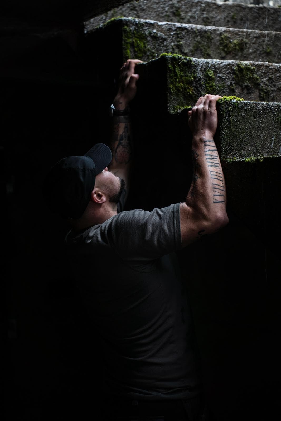Homme s'agrippant à un mur de béton couvert de mousse, lumière basse