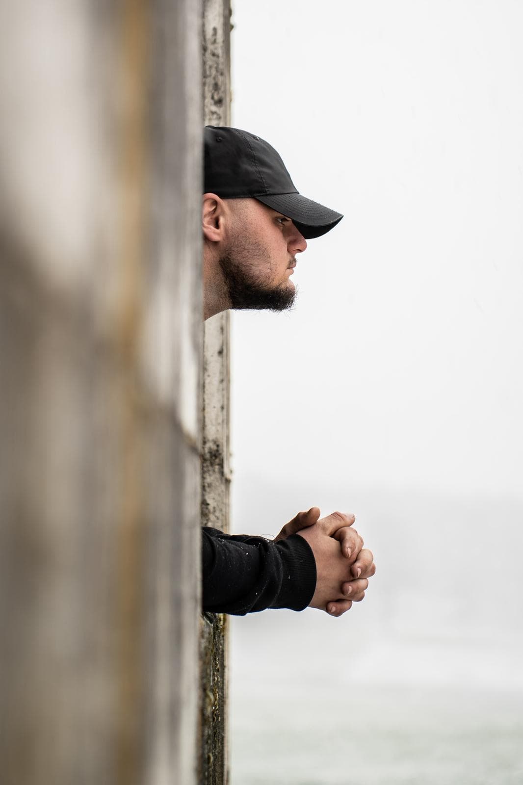Profil d'un homme à casquette derrière un poteau de bois, décor hivernal