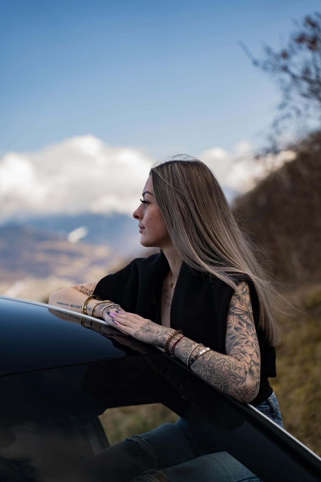 Portrait d'une personne accoudée au capot d'une voiture, paysage de montagne en arrière-plan